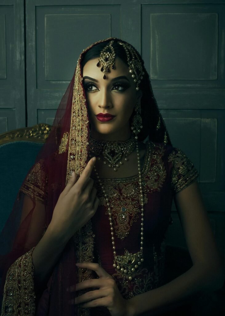 Silk Organza Zari Party Saree – Kerala Gold | Party Wear Kochi Stunning portrait of a woman wearing intricate traditional jewelry and maroon sari, exuding elegance and grace.